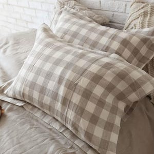May include: Two rectangular pillowcases featuring a beige and white checked pattern. The fabric has a visible woven texture, and each pillowcase is finished with a wide flange border along the edges, creating a structured look on the bed.