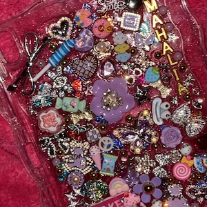 Könnte beinhalten: Eine transparente Handyhülle, gefüllt mit einer Vielzahl von Charms und Verzierungen. Die Hülle ist mit verschiedenen Formen wie Herzen, Blumen, Schleifen und Sternen in Rosa, Lila und Silber verziert. Der Text "MAKE MONEY WHILE SLEEPING" ist zu sehen.