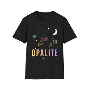 Pode incluir: T-shirt preto com um design celestial. A camisa apresenta o texto "BUT NOW THE SKY IS OPALITE" em uma fonte colorida e caprichosa, junto com uma lua crescente e estrelas.