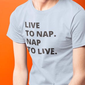 Könnte beinhalten: Hellblaues T-Shirt mit dem Aufdruck "LIVE TO NAP. NAP TO LIVE." in Schwarz.
