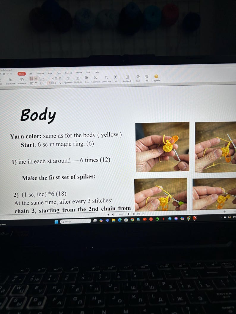 May include: A laptop screen displaying crochet instructions with the word "Body" at the top. The instructions include steps for creating spikes. Several images illustrate the crochet process. Colorful yarn balls are visible in the background.