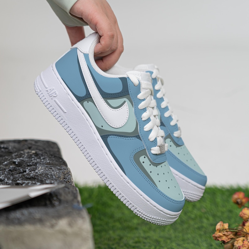 Puede incluir: Un par de zapatillas bajas azules y blancas con estampado de camuflaje. Las zapatillas tienen un logotipo Swoosh blanco y una suela blanca.