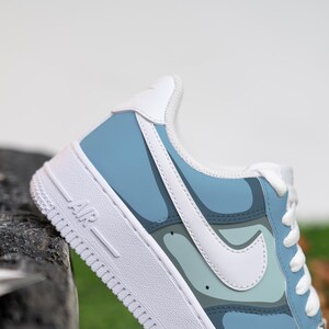 Puede incluir: Un par de zapatillas blancas y azules con un patr&oacute;n abstracto azul y blanco. Las zapatillas tienen un logotipo swoosh blanco y la palabra "AIR" impresa en el lateral.