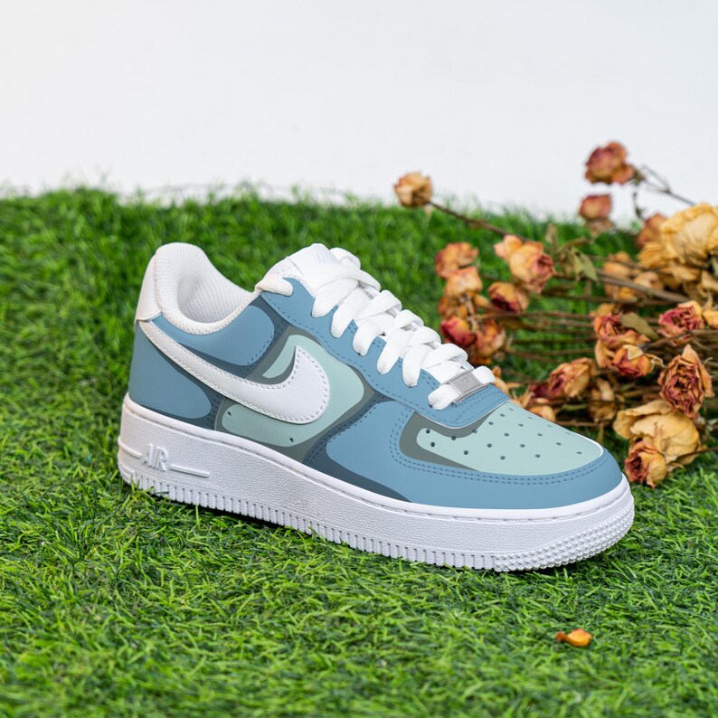 Puede incluir: Un par de zapatillas azules y blancas con un dise&ntilde;o abstracto &uacute;nico. Las zapatillas tienen una suela blanca y un logotipo swoosh blanco en el lateral.