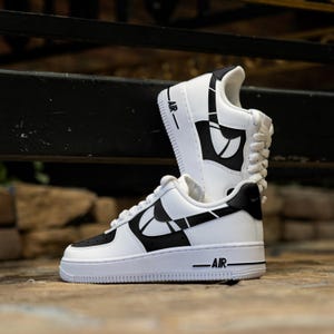 May include: White and black custom designed Nike Air Force 1 sneakers with a geometric pattern. The sneakers have the word "AIR" printed on the side.