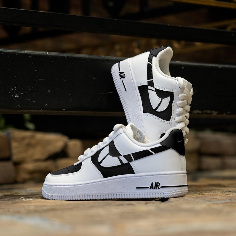 May include: White and black custom designed Nike Air Force 1 sneakers with a geometric pattern. The sneakers have the word "AIR" printed on the side.