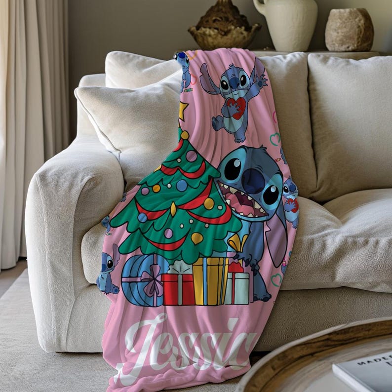 May include: Pink fleece throw blanket with a Christmas tree, presents, and Stitch from Lilo & Stitch. The blanket has the name "Jessie" printed on it.