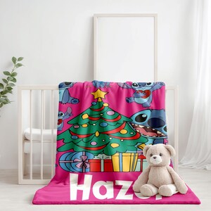 May include: Pink fleece blanket with a Christmas tree and Stitch characters. The blanket has the name "Haz" printed on it.