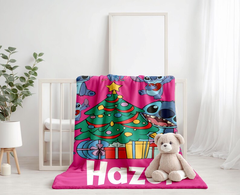 May include: Pink fleece blanket with a Christmas tree and Stitch characters. The blanket has the name "Haz" printed on it.