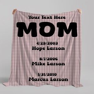 May include: Pink and black checkered blanket with the word "MOM" in large black letters. The text "Your Text Here" is at the top of the blanket. Below the word "MOM" are the names and dates of birth of three people: Hope Larson (4/29/2003), Mike Larson (8/7/2006), and Marcus Larson (1/31/2010).