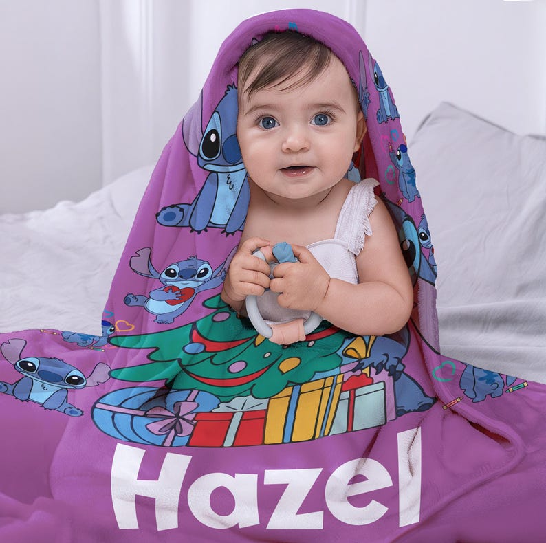 May include: Purple baby blanket with a Christmas tree and Stitch characters. The blanket has the name "Hazel" printed on it.