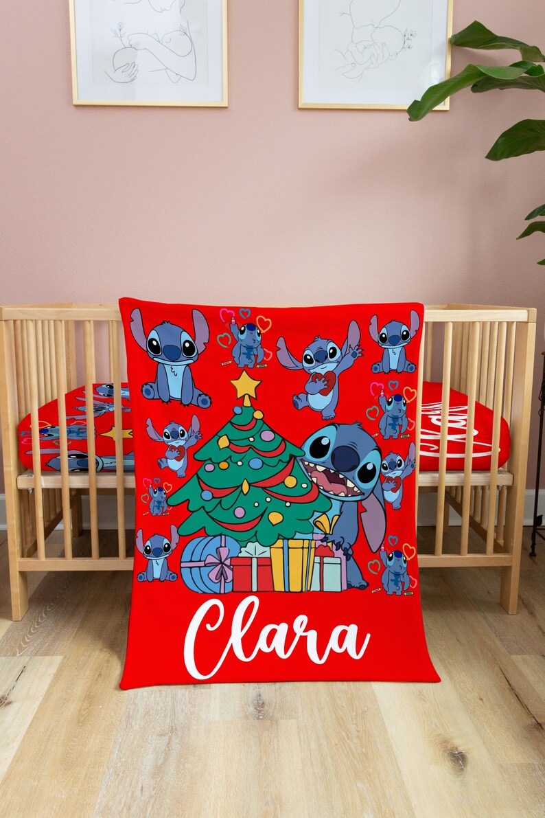 May include: Red and green Christmas themed blanket with a blue Stitch character from Lilo & Stitch holding a Christmas tree. The blanket has a white name "Clara" on the bottom.