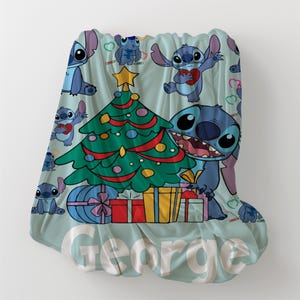 May include: A blue and green Christmas themed fleece blanket with a cartoon Stitch character and the name "George" printed on it.