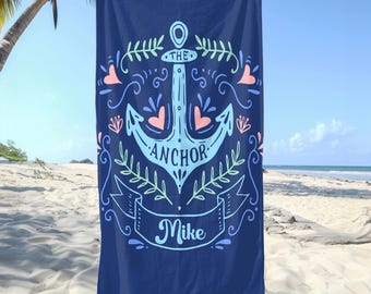 May include: A navy blue beach towel with a white anchor and the text "The Anchor Mike" in a decorative font. The anchor is surrounded by pink hearts and green leaves.
