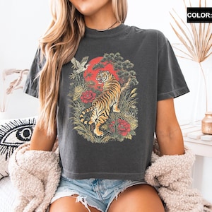 May include: Dark grey t-shirt featuring a tiger design with a red sun, flowers, and a bird. The shirt is a crew neck and has short sleeves. The color is pepper.