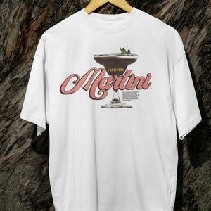 Puede incluir: Camiseta blanca con un dise&ntilde;o de Espresso Martini. El dise&ntilde;o incluye una ilustraci&oacute;n de c&oacute;ctel con la palabra "Espresso" arriba y "Martini" en una fuente estilizada. Una ramita de menta corona la bebida.