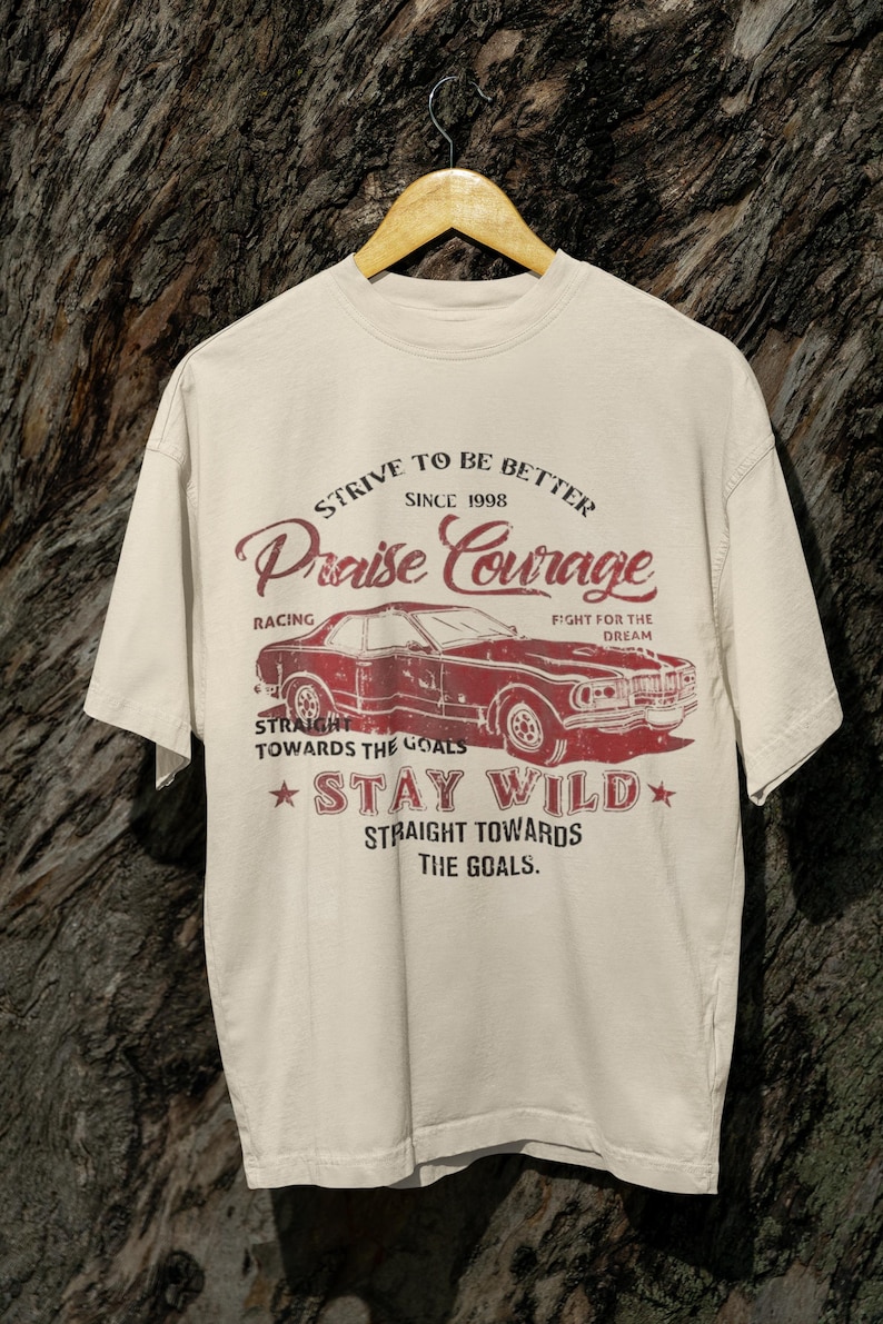 K&ouml;nnte beinhalten: Ein beiges T-Shirt mit einem roten Vintage-Auto-Motiv und dem Text "Strive to be better since 1998 Praise Courage Racing Fight for the Dream Straight towards the goals Stay Wild Straight towards the goals."