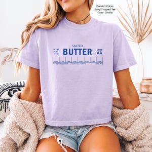 Puede incluir: Camiseta Comfort Colors color orqu&iacute;dea, corte holgado y corto, con el texto "SALTED BUTTER AA" y una gu&iacute;a de medidas. El peso neto de la camiseta es de 113g.
