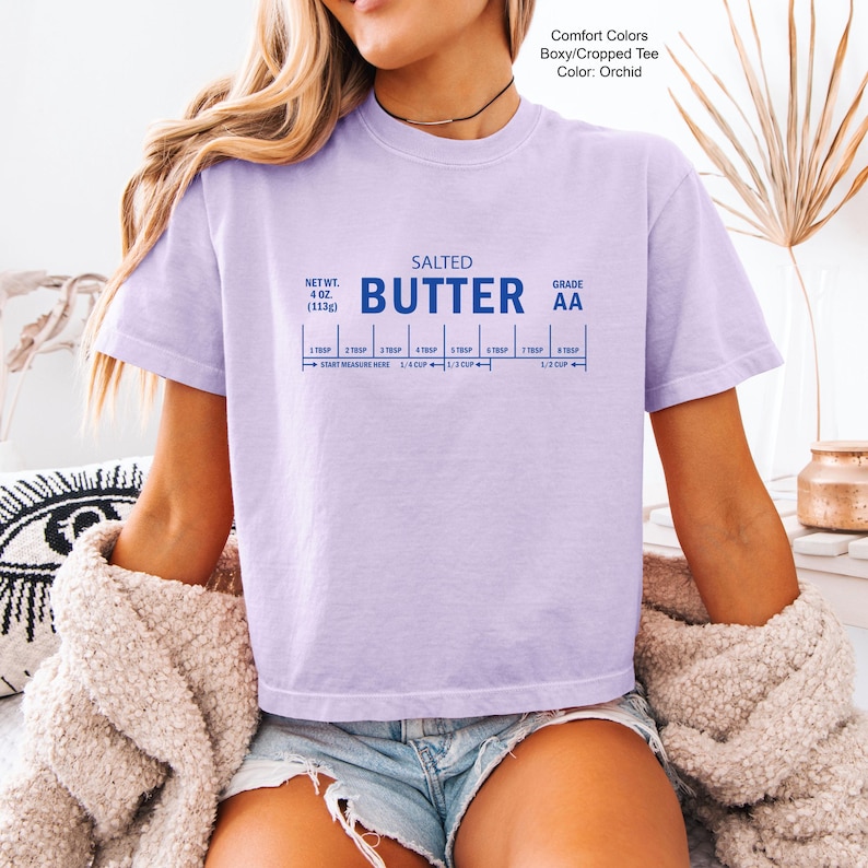 Puede incluir: Camiseta Comfort Colors color orqu&iacute;dea, corte holgado y corto, con el texto "SALTED BUTTER AA" y una gu&iacute;a de medidas. El peso neto de la camiseta es de 113g.