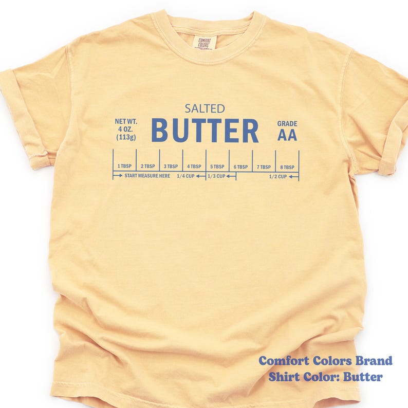 May include: Butter-colored t-shirt with the word "BUTTER" in large blue letters. The shirt also features text indicating net weight, grade, and measurement markings for butter, including "4 OZ. (113g)" and "1/2 CUP".