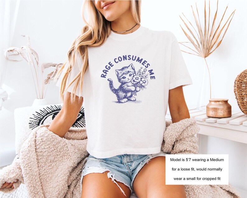 May include: White t-shirt with a blue illustration of a kitten holding flowers, and the text "RAGE CONSUMES ME" in a circular design. The shirt is a casual style.