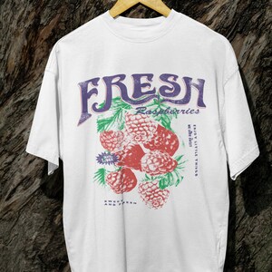 May include: White t-shirt with a graphic print of raspberries and the text "FRESH Raspberries Enjoy Little Things While They Last Sweet & Fresh & Tasty".