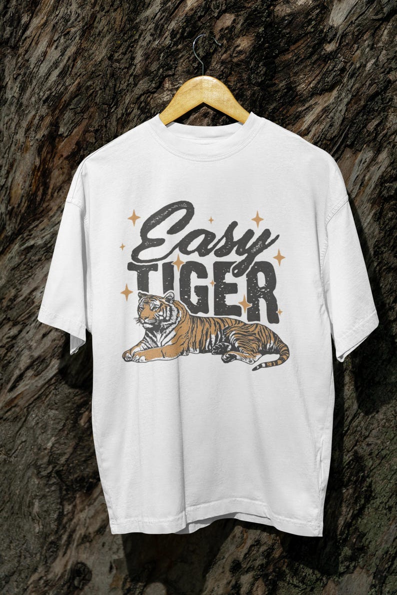 K&ouml;nnte beinhalten: Wei&szlig;es T-Shirt mit dem Text "Easy Tiger" im Vintage-Stil, mit einer Tiger-Illustration. Der Tiger ist braun und schwarz und liegt. Das Design enth&auml;lt Sterne.