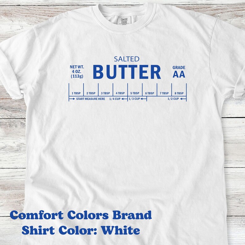 May include: White t-shirt with blue text and a butter measurement guide. The shirt features the words "SALTED BUTTER" and "GRADE AA". Measurements are in tablespoons and cups, with a net weight of 4 oz (113g). The shirt is a Comfort Colors brand.