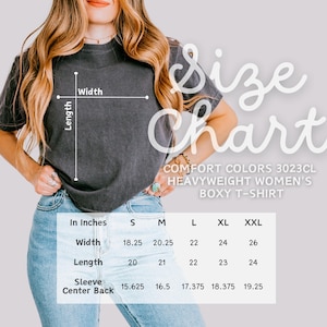 May include: A charcoal gray Comfort Colors 3023CL heavyweight boxy t-shirt. The image includes a size chart with measurements in inches for width, length, and sleeve center back. The chart shows sizes S, M, L, XL, and XXL.