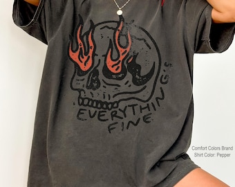 May include: Pepper-coloured t-shirt featuring a skull graphic with flames and the text "EVERYTHING FINE." The graphic is in black and red. The shirt is a Comfort Colors brand.