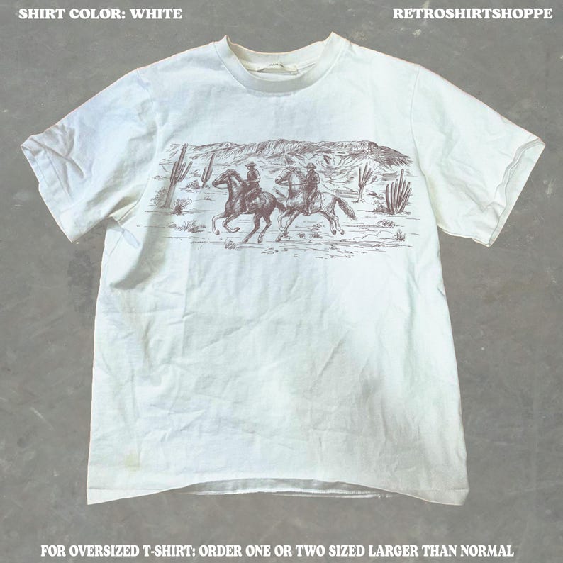 May include: White t-shirt featuring a sepia-toned graphic of two cowboys riding horses through a desert landscape with cacti and mountains. The text "RETROSHIRTSHOPPE" is at the top. The text "SHIRT COLOR: WHITE" is at the top. The text "FOR OVERSIZED T-SHIRT: ORDER ONE OR TWO SIZED LARGER THAN NORMAL" is at the bottom.