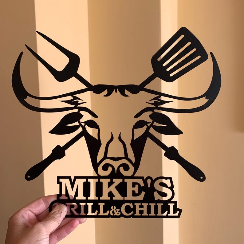 Black metal wall art featuring a bull's head with crossed grilling tools and the text "MIKE'S GRILL & CHILL".