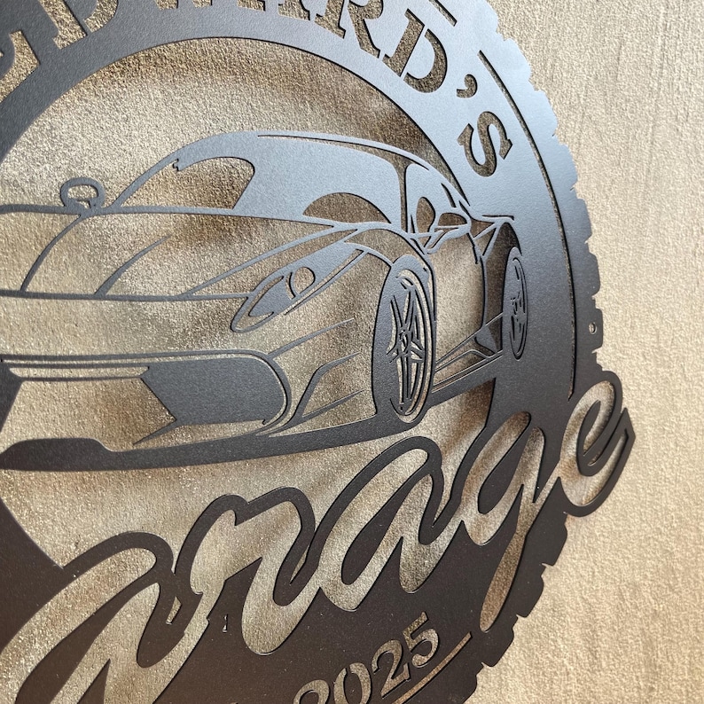 Op de afbeelding: Zwart metalen bord met een silhouet van een sportwagen en de tekst "[Name]'s Garage" met het jaar 2025 eronder.