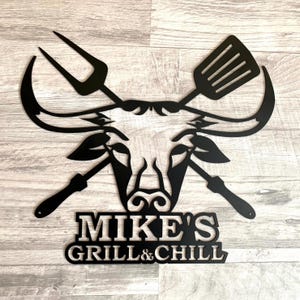 Black metal wall art featuring a bull's head with crossed grilling tools and the text "MIKE'S GRILL & CHILL".