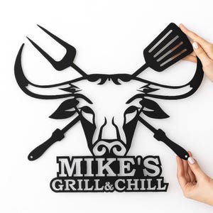 Custom metal BBQ name sign with bull head and grilling tools, personalized wall decor for outdoor kitchen.