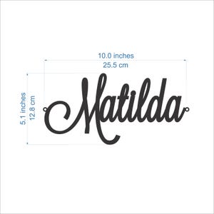 May include: A black script-style wall sign displaying the name Matilda, featuring small circular loops on each end. The sign measures 10.0 inches in width and 5.1 inches in height, as indicated by the visible measurement lines and text.