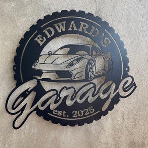 Op de afbeelding: Zwart metalen bord met een bandenprofielontwerp, met een witte sportwagen en de tekst "Edward's Garage est. 2025".