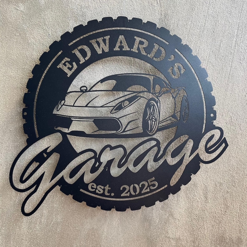 Op de afbeelding: Zwart metalen bord met een bandenprofielontwerp, met een witte sportwagen en de tekst "Edward's Garage est. 2025".
