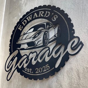 Op de afbeelding: Zwart metalen bord met een bandenprofielrand, met een gestileerde auto en de tekst "Edward's Garage est. 2025".
