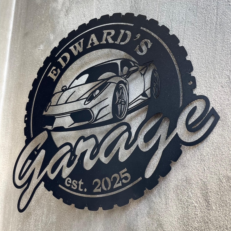 Op de afbeelding: Zwart metalen bord met een bandenprofielrand, met een gestileerde auto en de tekst "Edward's Garage est. 2025".