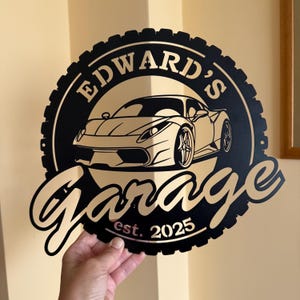 Op de afbeelding: Zwart metalen bord met een bandenprofiel, met een witte sportwagen en de tekst "Edward's Garage est. 2025".