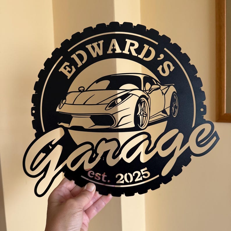 Op de afbeelding: Zwart metalen bord met een bandenprofiel, met een witte sportwagen en de tekst "Edward's Garage est. 2025".