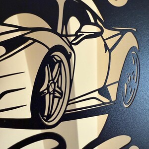 Op de afbeelding: Zwarte en gouden silhouet van een sportwagen met een gedetailleerd ontwerp van de wielen en de carrosserie. De auto is naar de rechterkant van de afbeelding gericht.