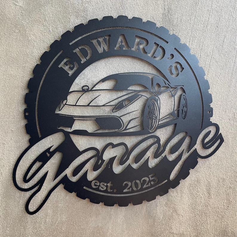 Op de afbeelding: Zwart metalen bord met een bandenprofiel, met een silhouet van een sportwagen en de tekst "Edward's Garage est. 2025".