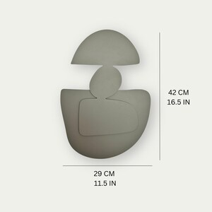 May include: A gray ceramic wall sculpture with an abstract design. The sculpture is 16.5 inches tall and 11.5 inches wide.