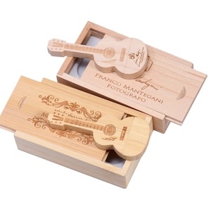 May include: Two wooden boxes with guitar-shaped USB drives inside. The boxes are made of light brown wood and have a natural finish. The USB drives are engraved with a guitar design and the text "Franco Mantegani Fotografo".