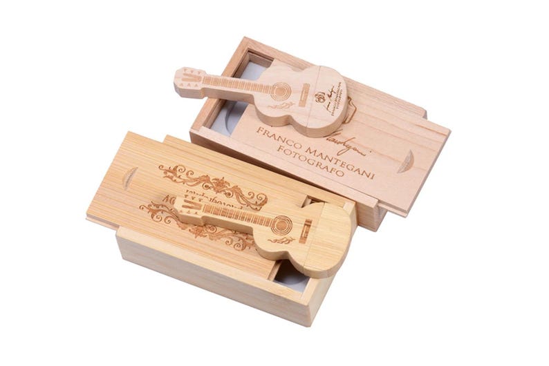 May include: Two wooden boxes with guitar-shaped USB drives inside. The boxes are made of light brown wood and have a natural finish. The USB drives are engraved with a guitar design and the text "Franco Mantegani Fotografo".