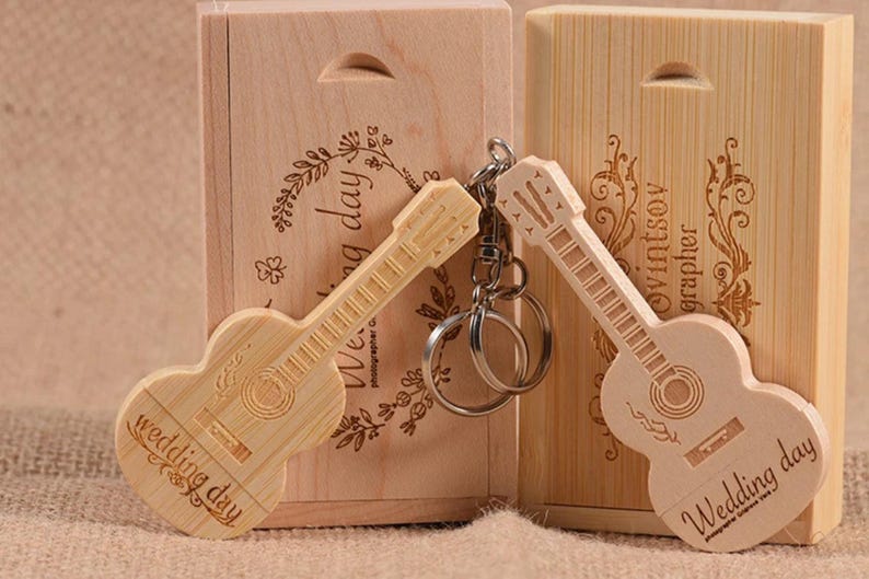 May include: Two wooden guitar-shaped USB drives with the text "Wedding day" engraved on them. The drives are in wooden boxes with engraved floral designs. One box has the text "Wedding day" engraved on it, and the other has the text "Photographer OwintSoy" engraved on it.
