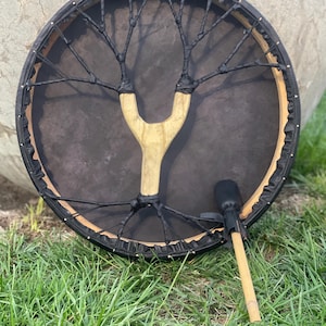 May include: A black and brown hand drum with a wooden handle and a black beater. The drum has a black leather head and a black rope design.