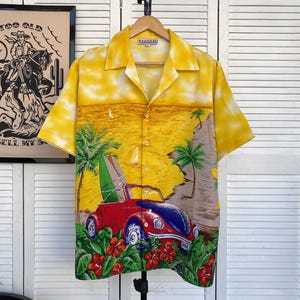May include: Yellow short-sleeved button-up shirt with a beach scene print. The print features a red convertible car with a surfboard on the roof, palm trees, and flowers. The shirt has a "Rivaldi" label.